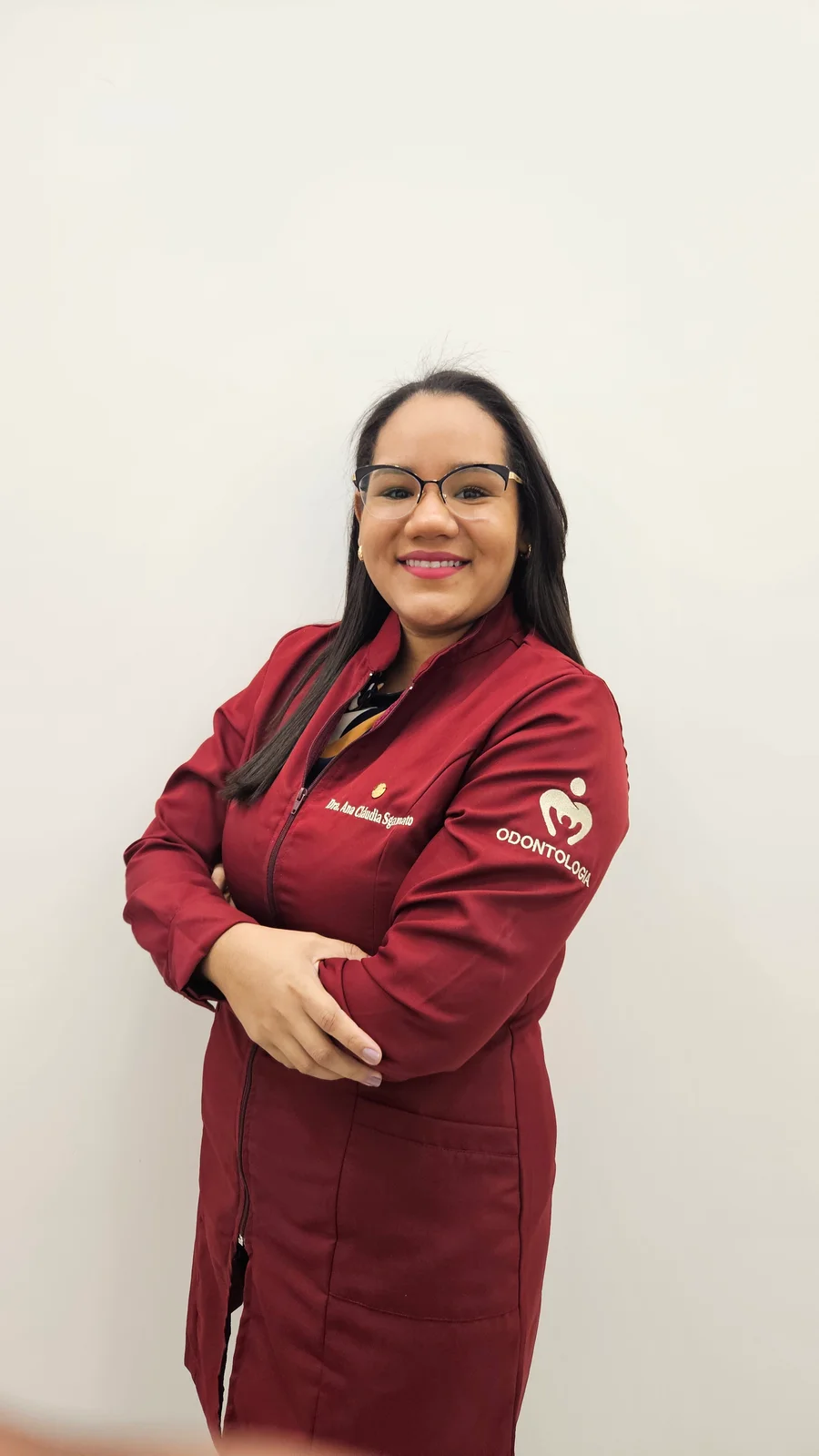 Dra. Ana Cláudia Sgamato, sorrindo e vestindo jaleco vinho